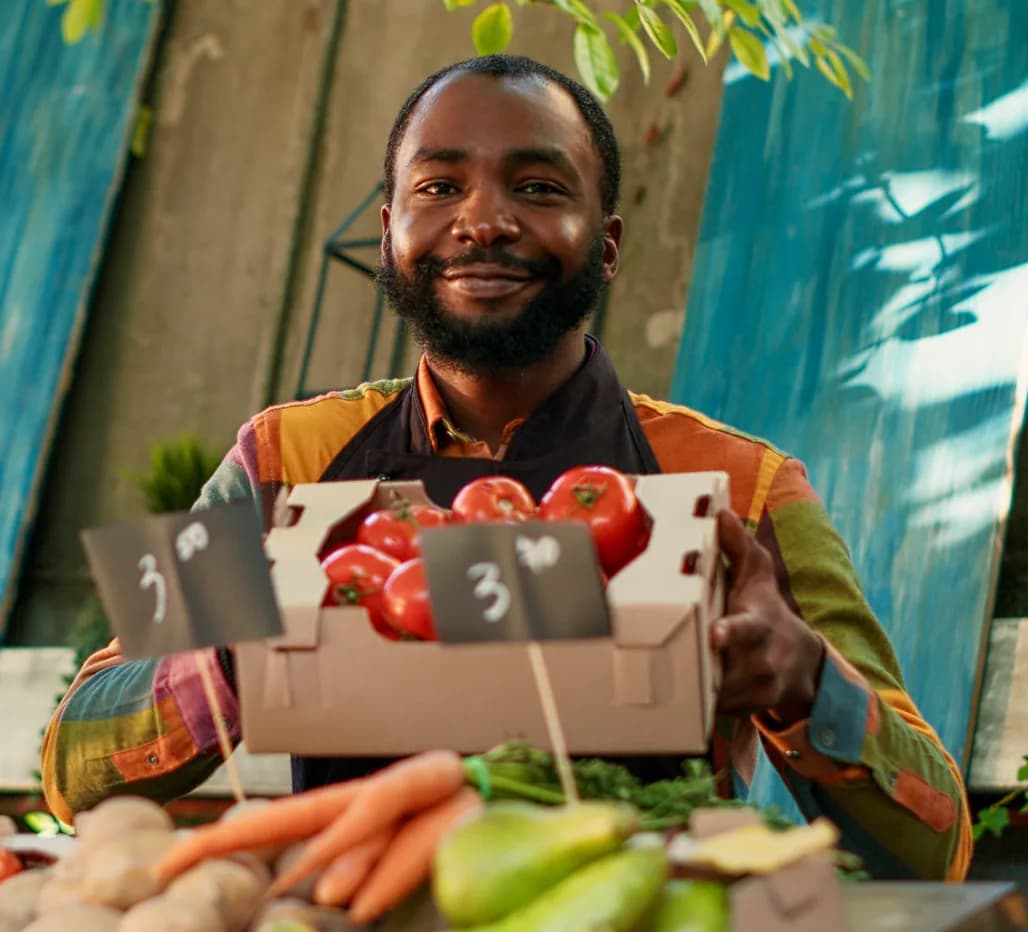 Smiling market trader holding a crate of tomatoes
